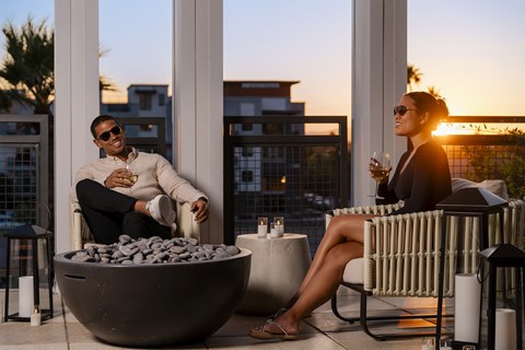 a man and a woman sitting on a roof terrace with wine glasses